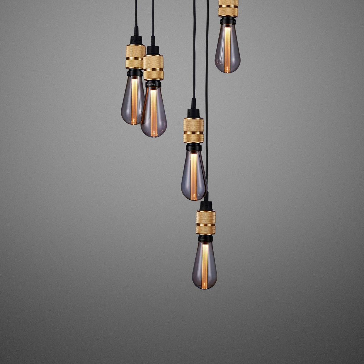 Five pendant lights with smoked glass bulbs and brass fittings hang against a grey background. 