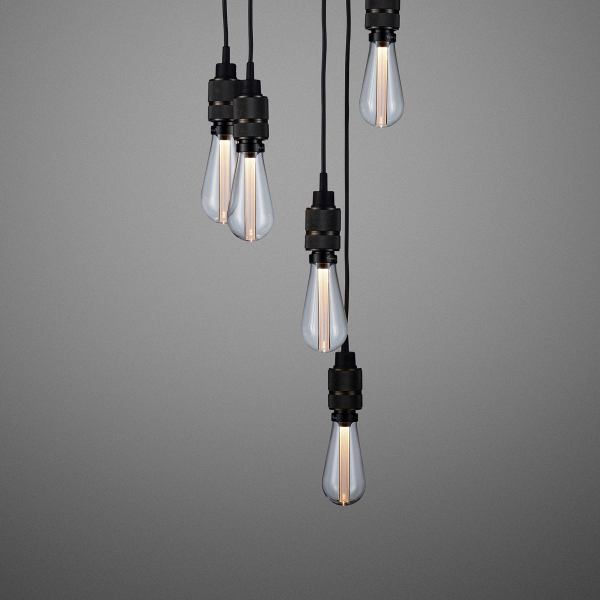 Five pendant light bulbs with clear glass and black bases hang against a gray background.