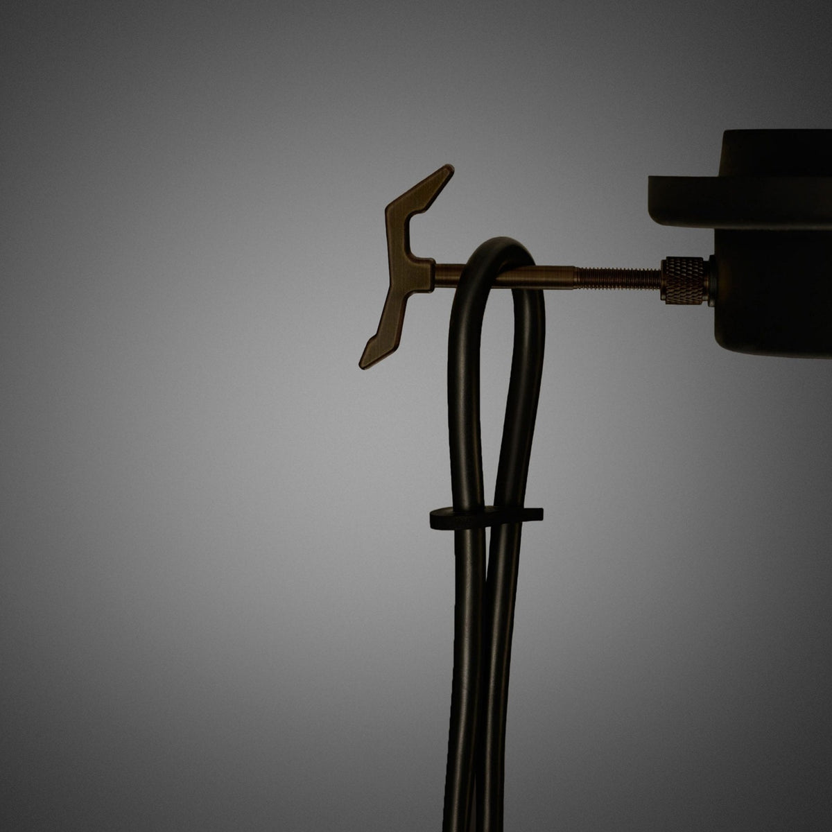 Close-up of a black cable looped and secured by a small black clip, with a brass-colored hook and screw mechanism.