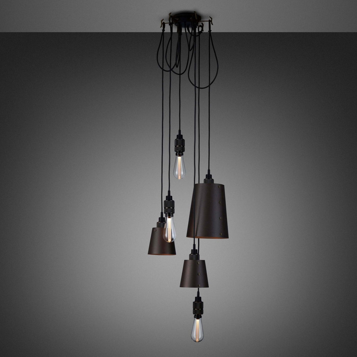 An array of dark metallic pendant lamps and bare bulbs hanging from a ceiling fixture.