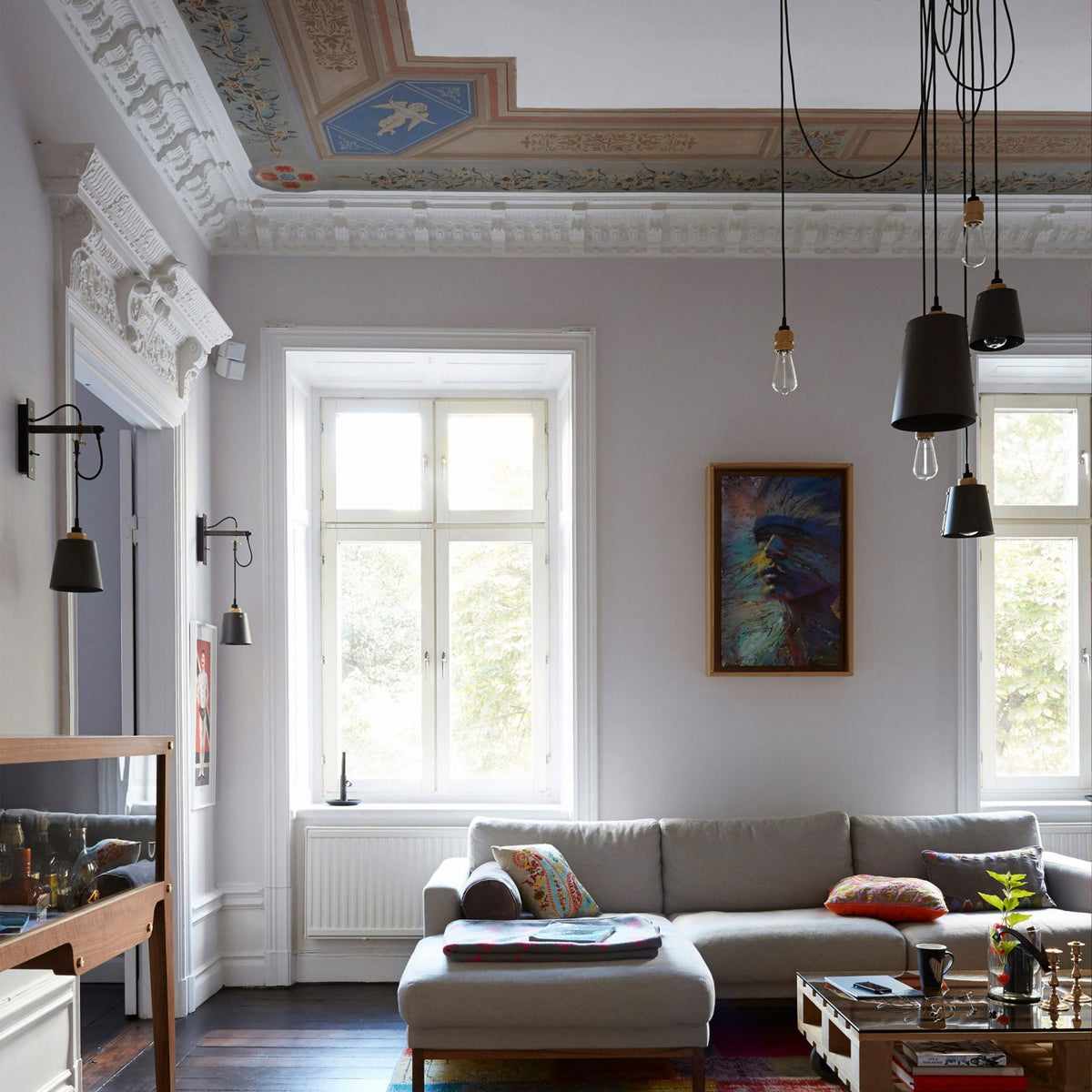 A living room with a grey sofa, large windows, and a multi-pendant ceiling light.