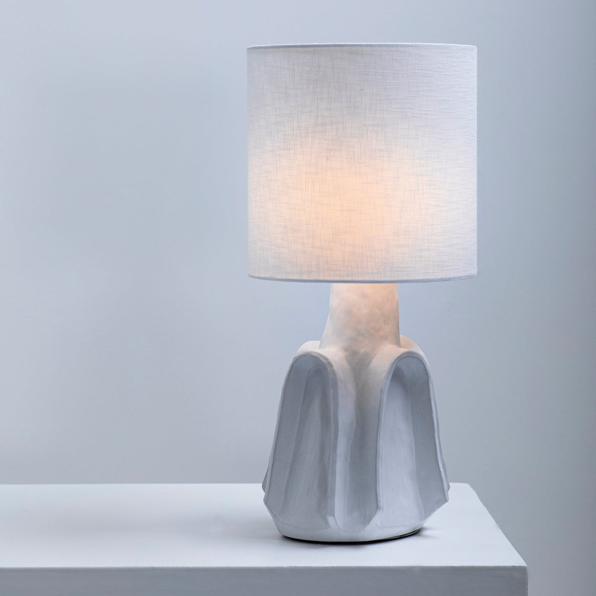 A white table lamp with a textured base and a simple, cylindrical shade on a white surface.