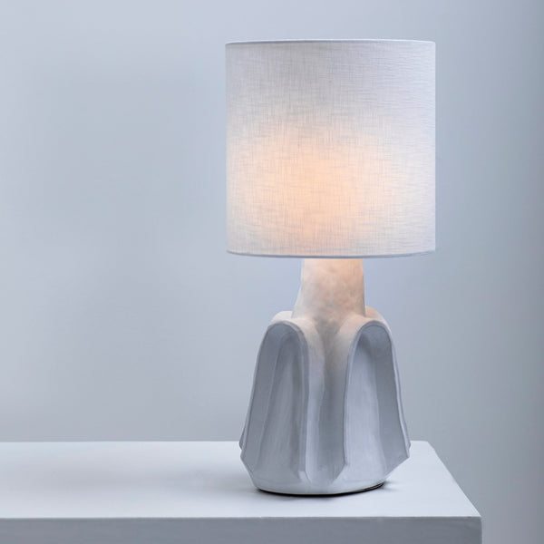 A white table lamp with a textured base and a simple, cylindrical shade on a white surface.