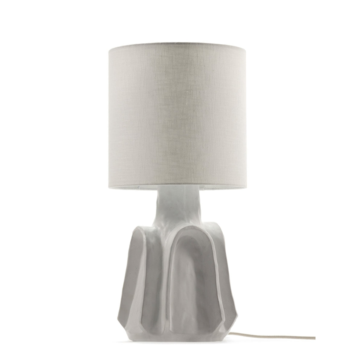 A white table lamp with a sculptural base and a light-coloured cylindrical shade against a white background.