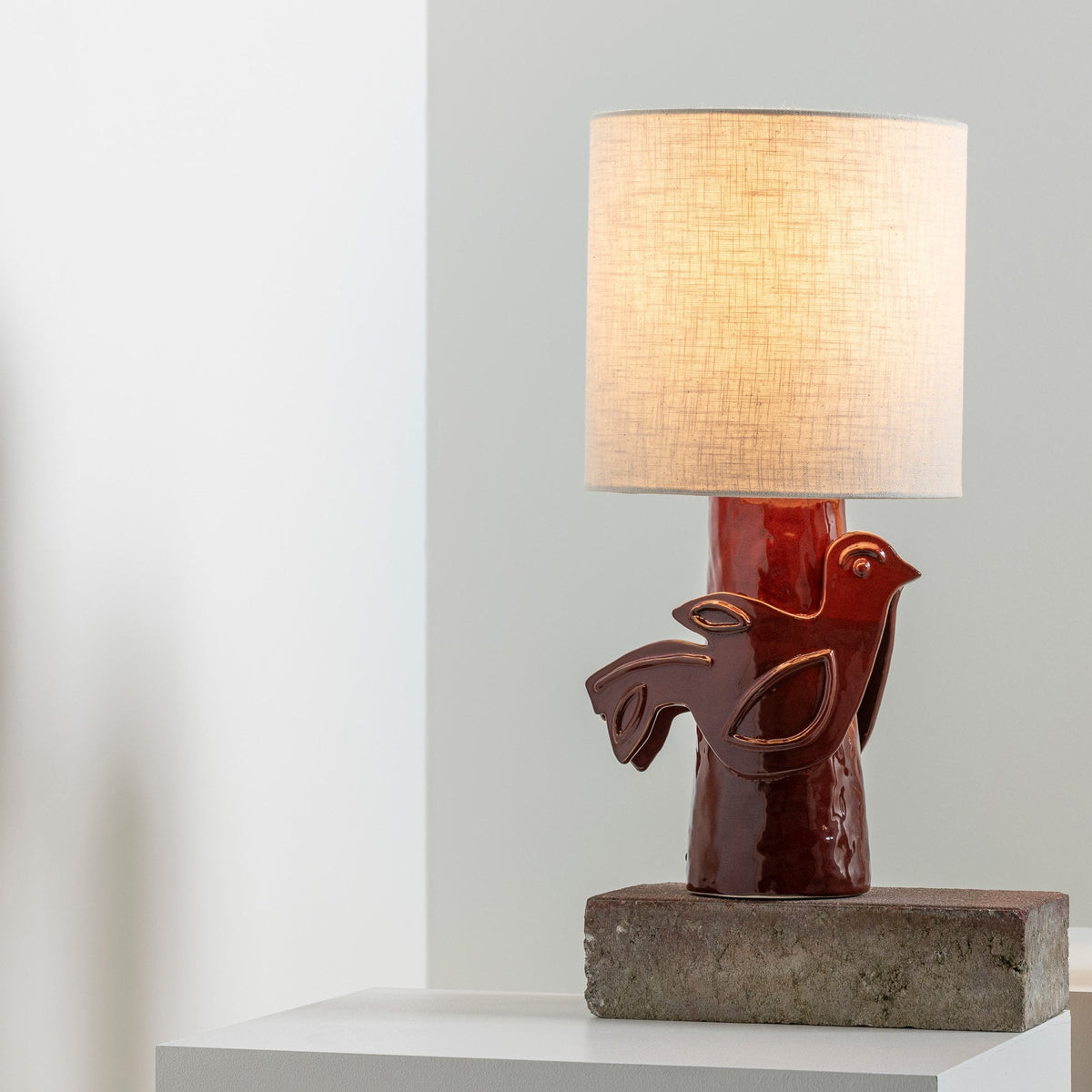 A decorative red ceramic lamp with a bird design and a fabric shade.