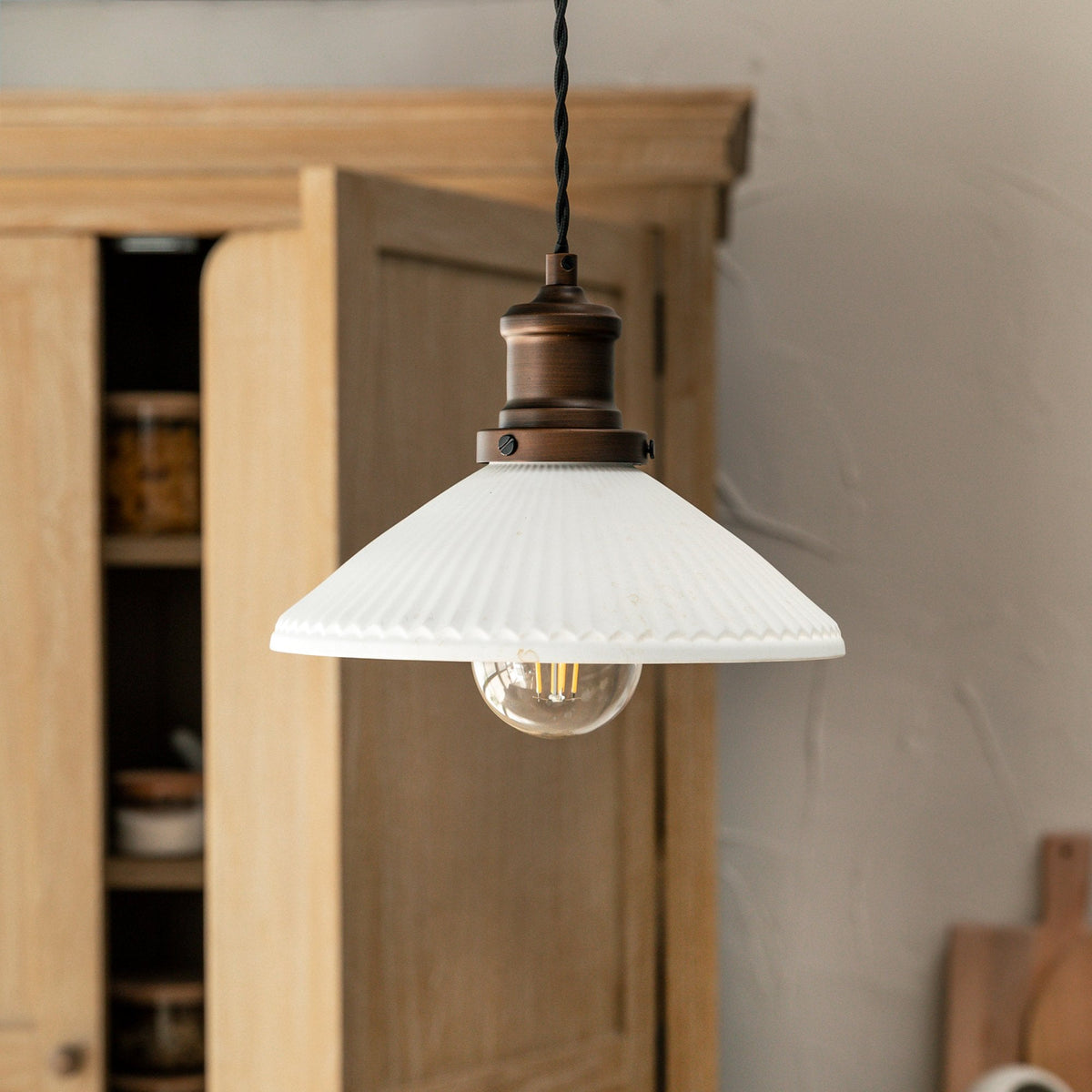 A white fluted glass pendant light with a bronze fixture and exposed bulb hangs in a kitchen.