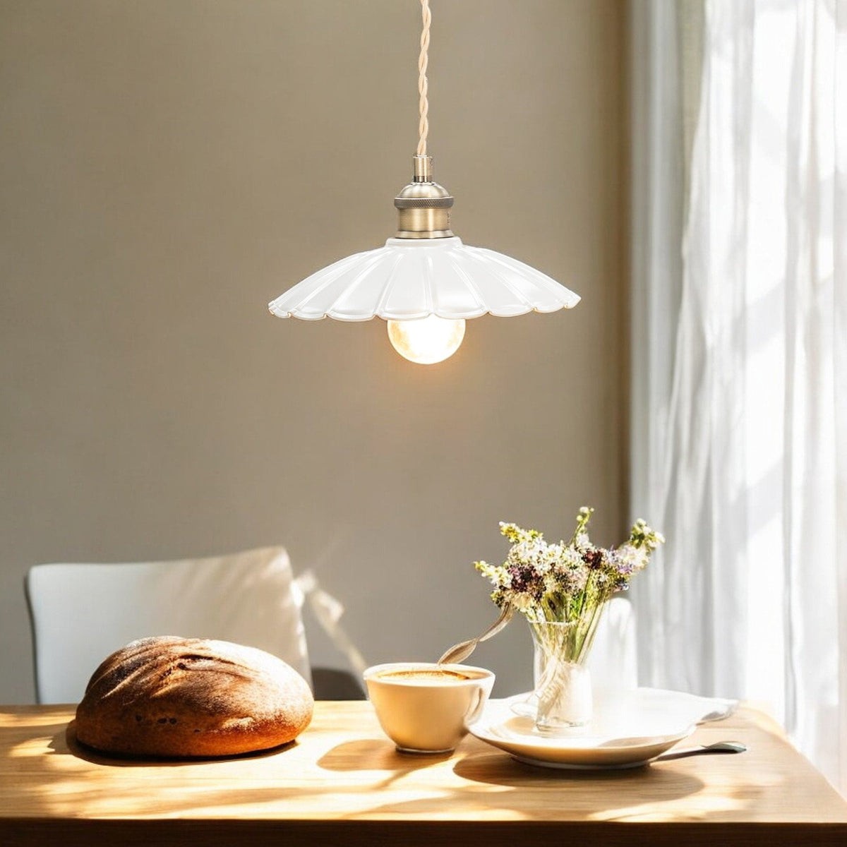 A white fluted pendant light illuminates a wooden table with bread, coffee, and flowers.