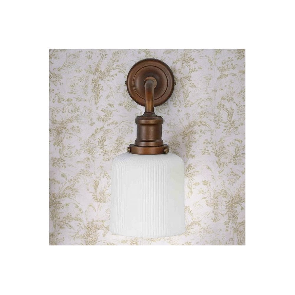Vintage bronze wall sconce with a ribbed white glass shade against floral wallpaper.