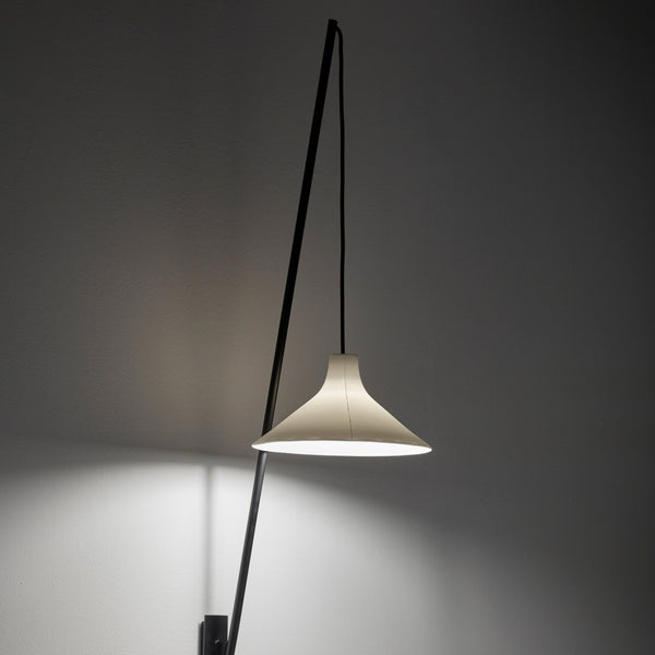 A white conical lampshade, emitting warm light, is suspended from an angled black arm.
