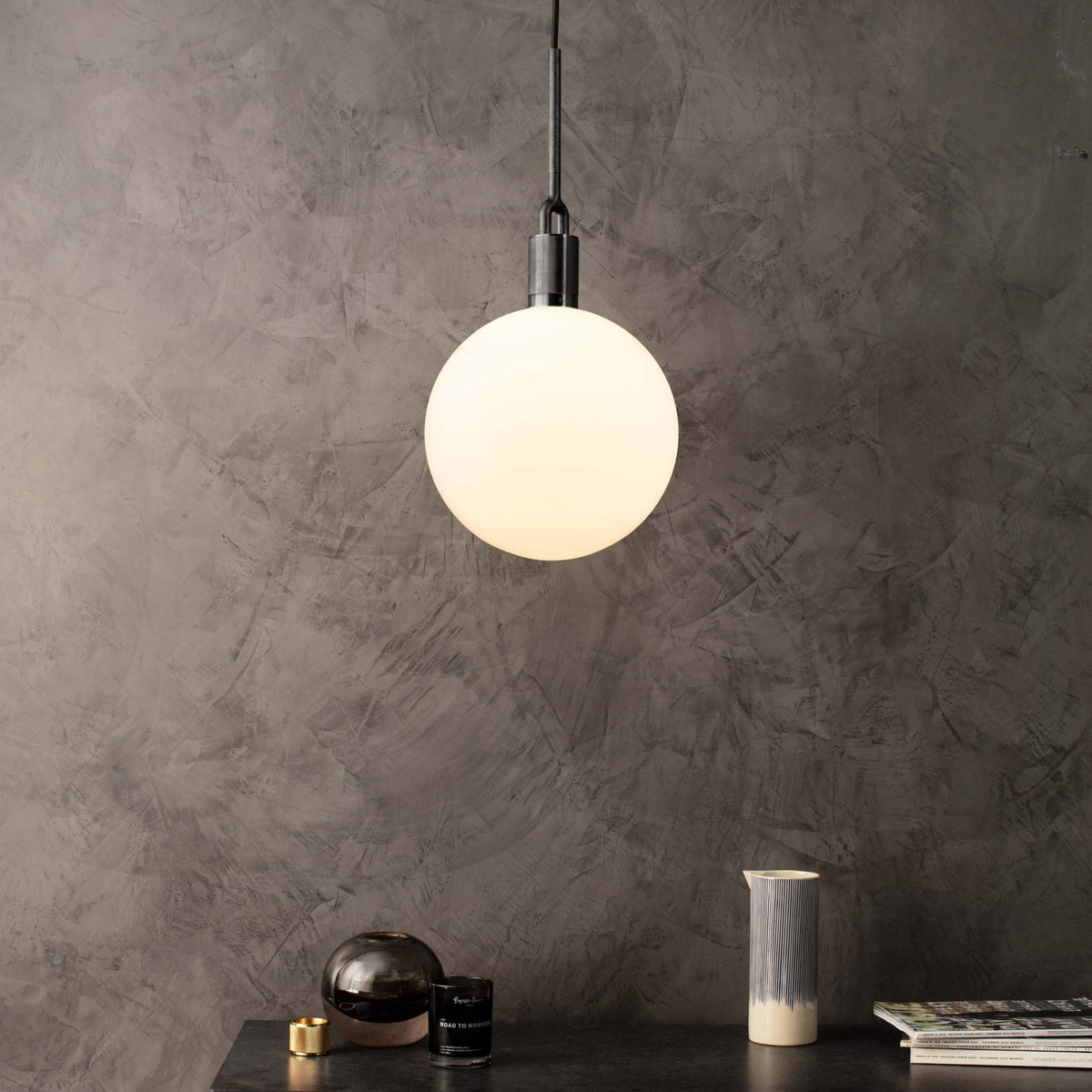 A white spherical pendant light hangs above a dark table with decorative items against a textured gray wall.