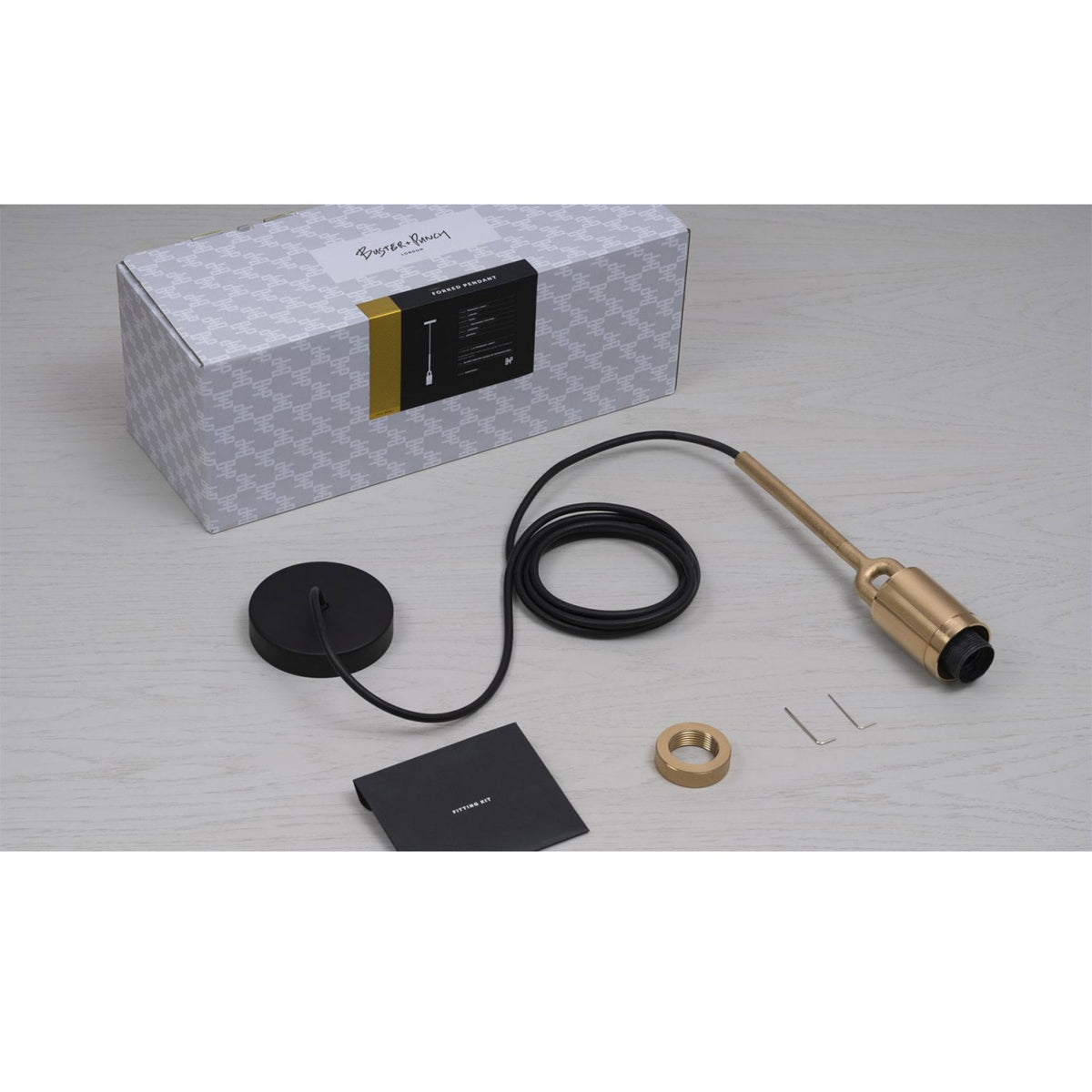 Buster + Punch pendant light kit with a gold pendant, black cord, and ceiling rose, alongside a patterned box.