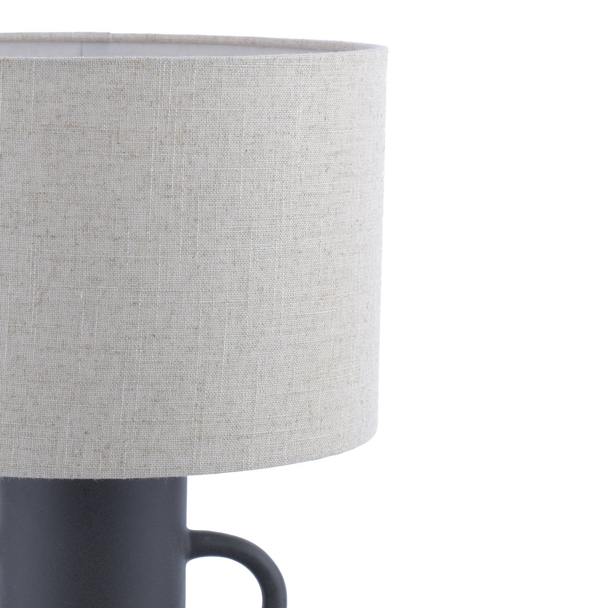 Close-up of the light fabric shade and part of the base of a dark grey amphora-shaped table lamp.