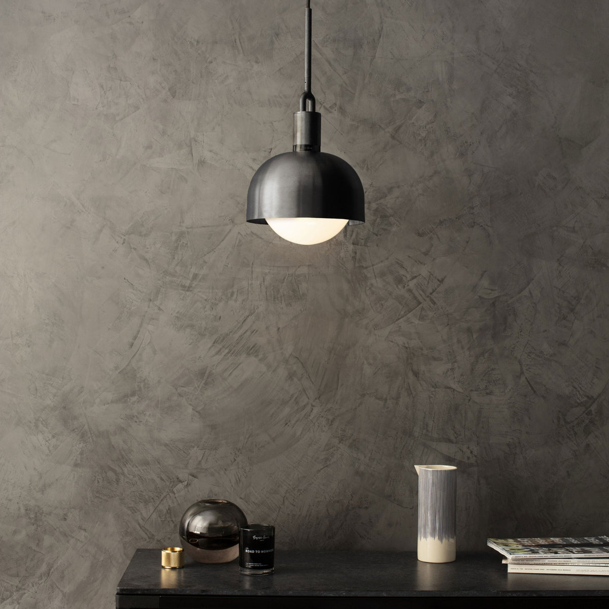 A modern black pendant light hangs above a dark countertop with decorative items and magazines.