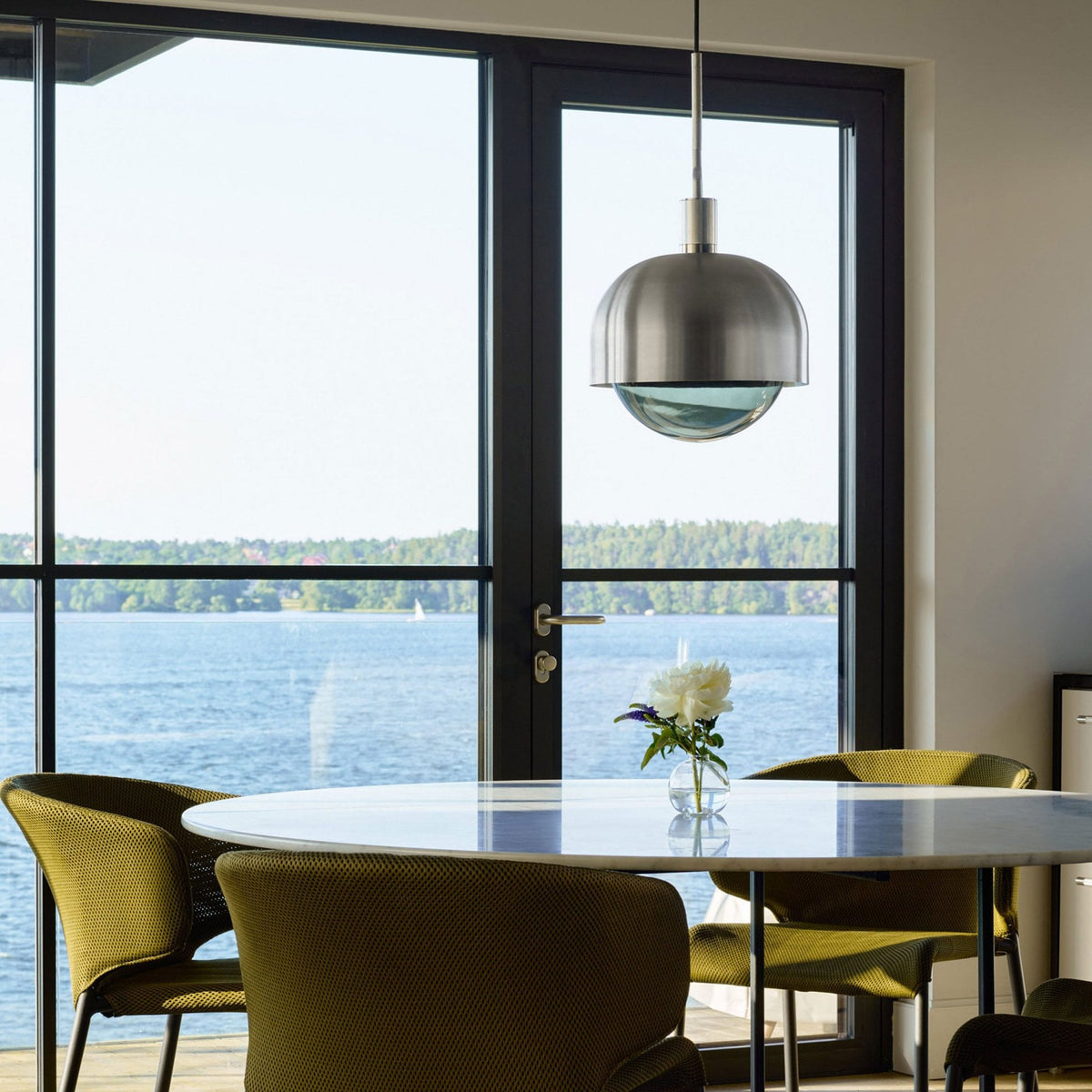 A modern dining room with a stainless steel pendant light, overlooking a lake.