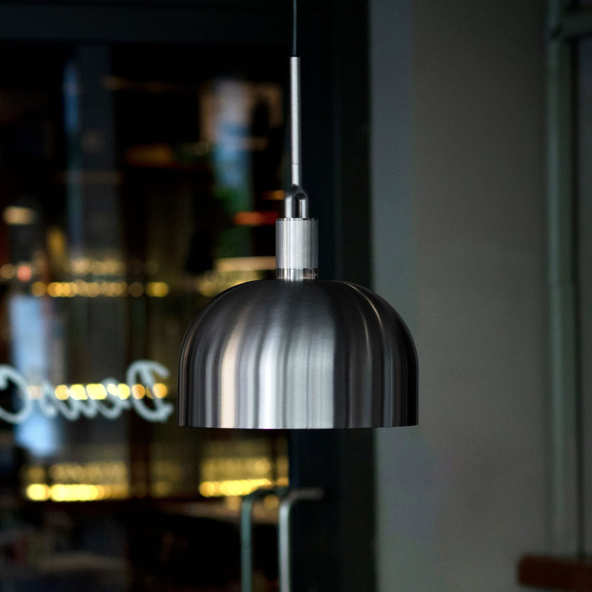 A brushed metal pendant light with a domed shade hangs from the ceiling, with blurred reflections in the background.