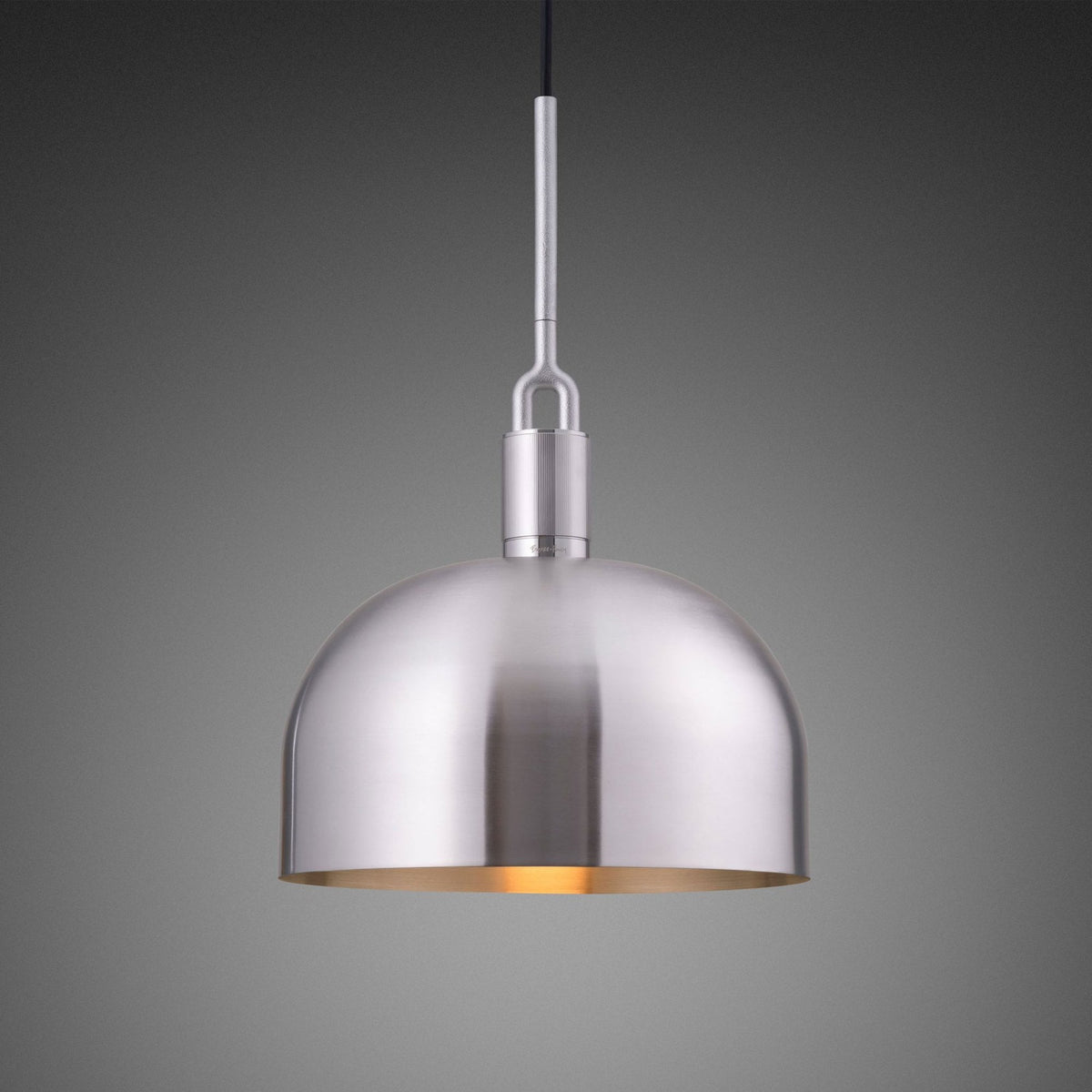 A brushed metal pendant light with a dome-shaped shade and a warm glow emanating from within. It hangs from a slender rod.