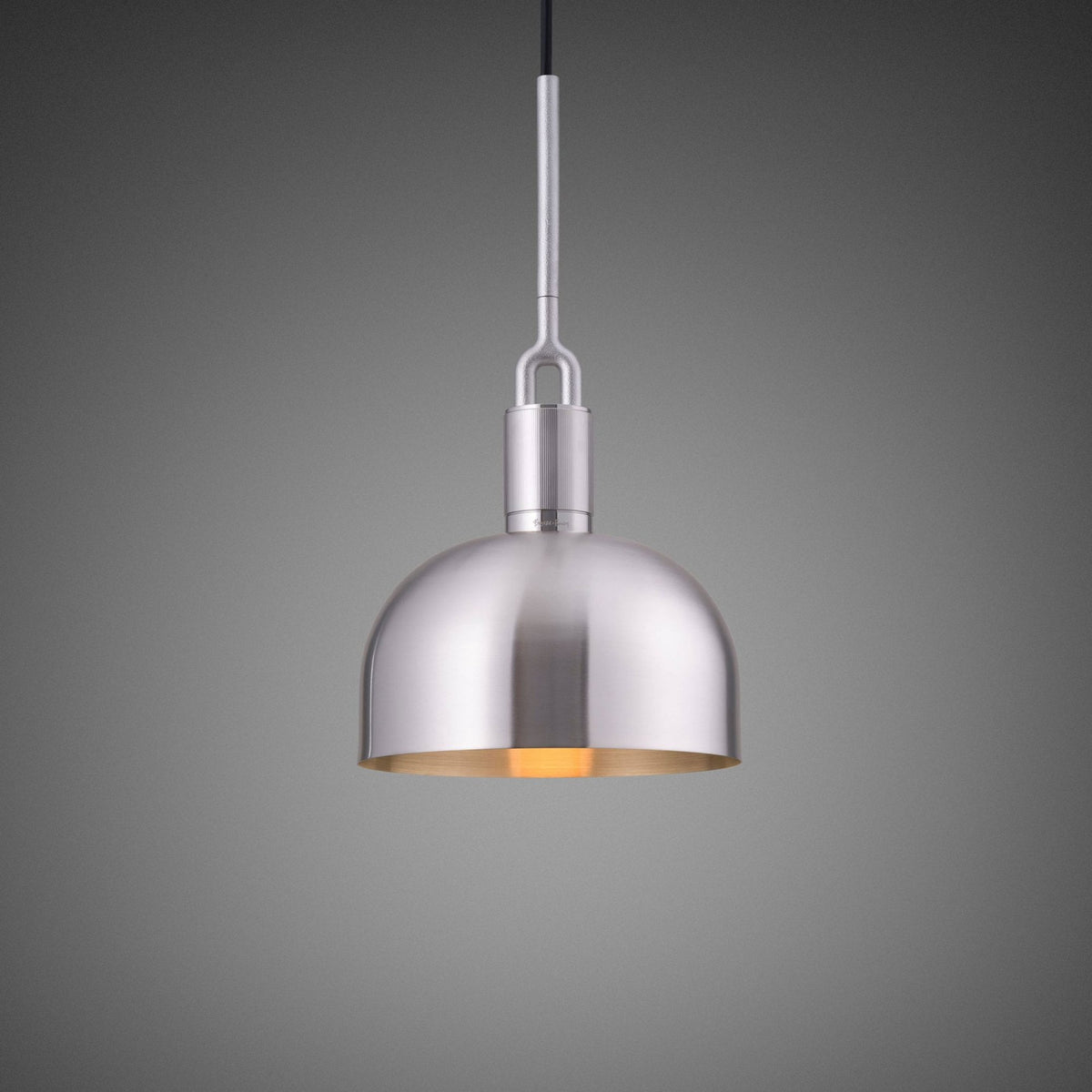 Brushed metal pendant light with a domed shade and a warm glow from within, hanging against a grey background.