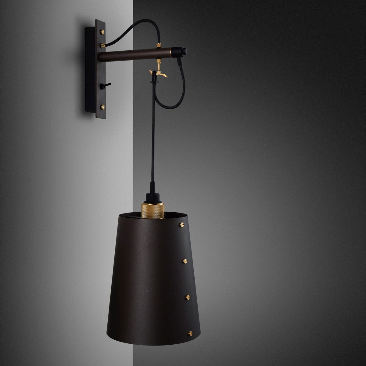 Black wall lamp with a conical shade and brass accents, mounted on a grey wall.