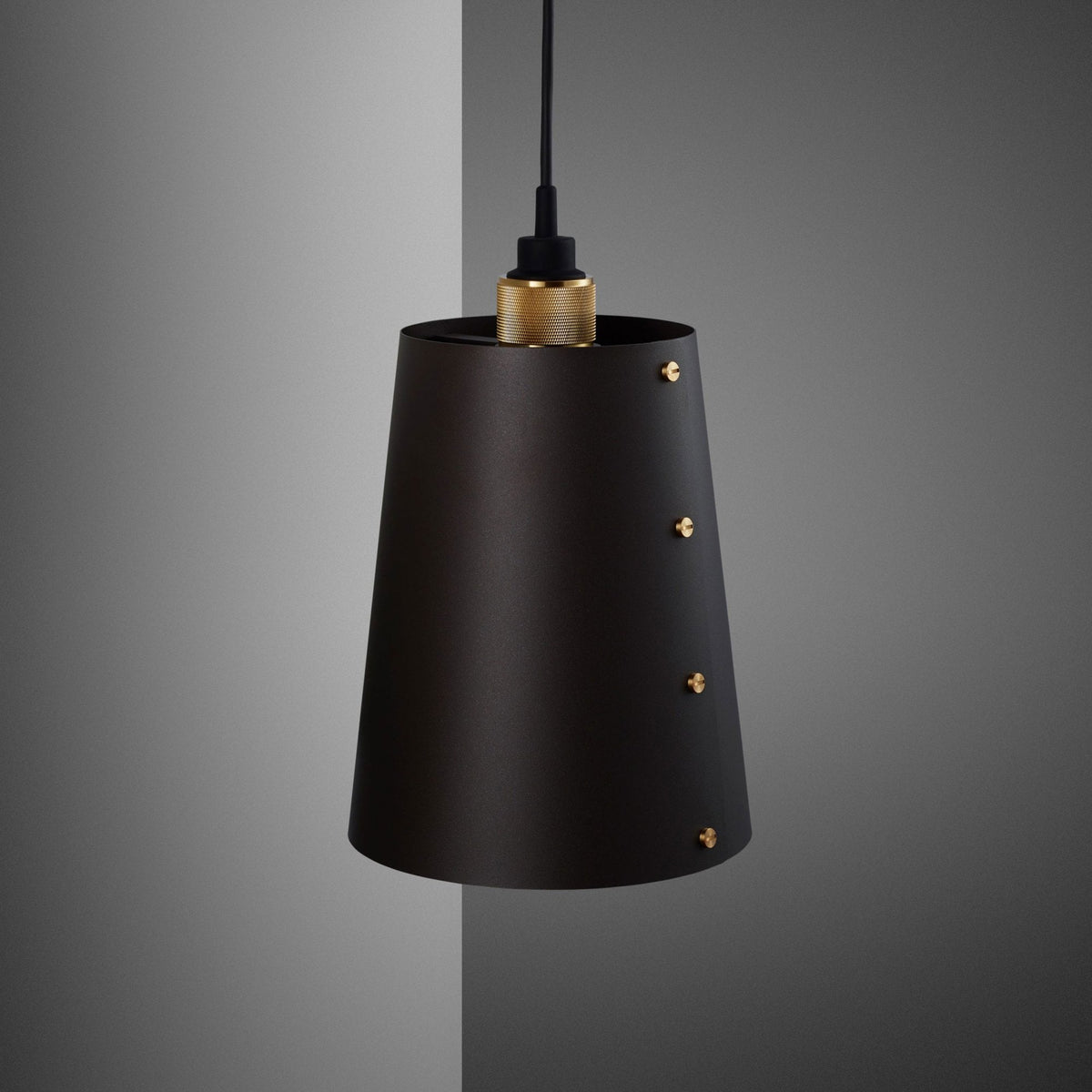 Black conical pendant light with brass details hanging against a grey wall.