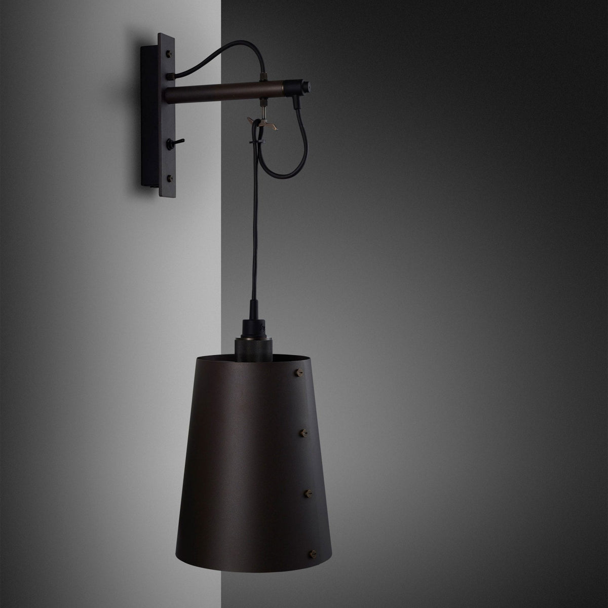A close-up of a wall-mounted light fixture with a cone-shaped black shade.