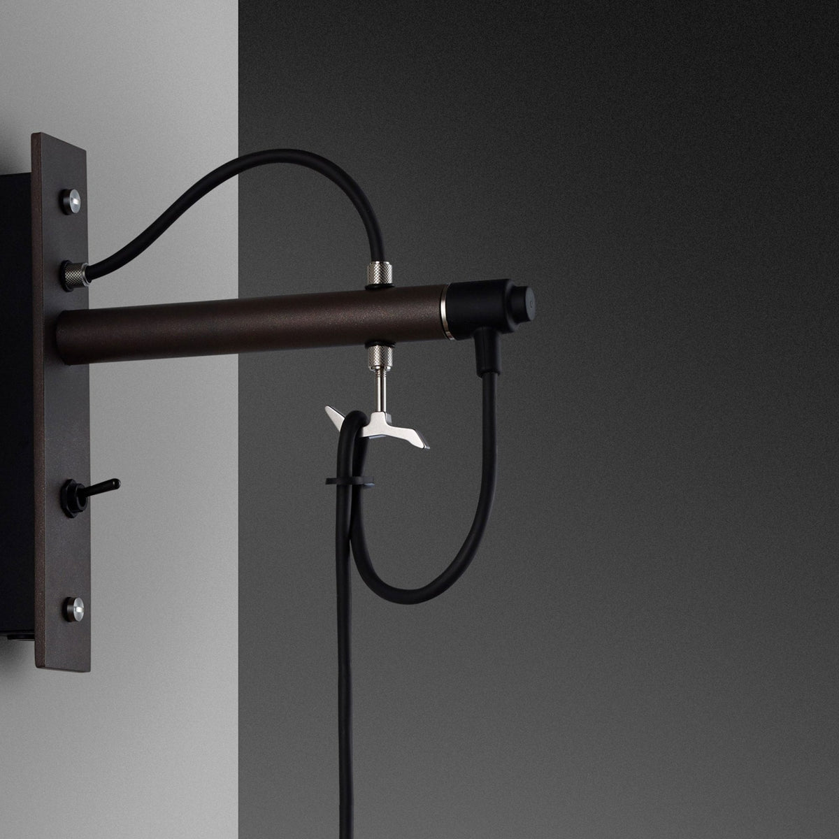 Close-up of a wall-mounted light fixture with a brown cylindrical arm, black cables, and a toggle switch.