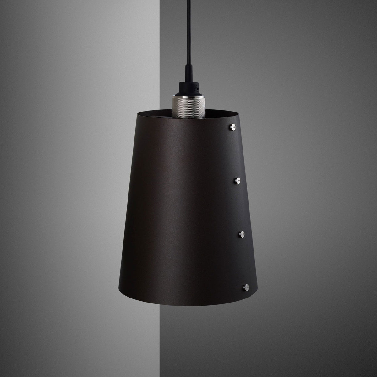 A black pendant light with a conical shade and silver accents, hanging against a grey wall.