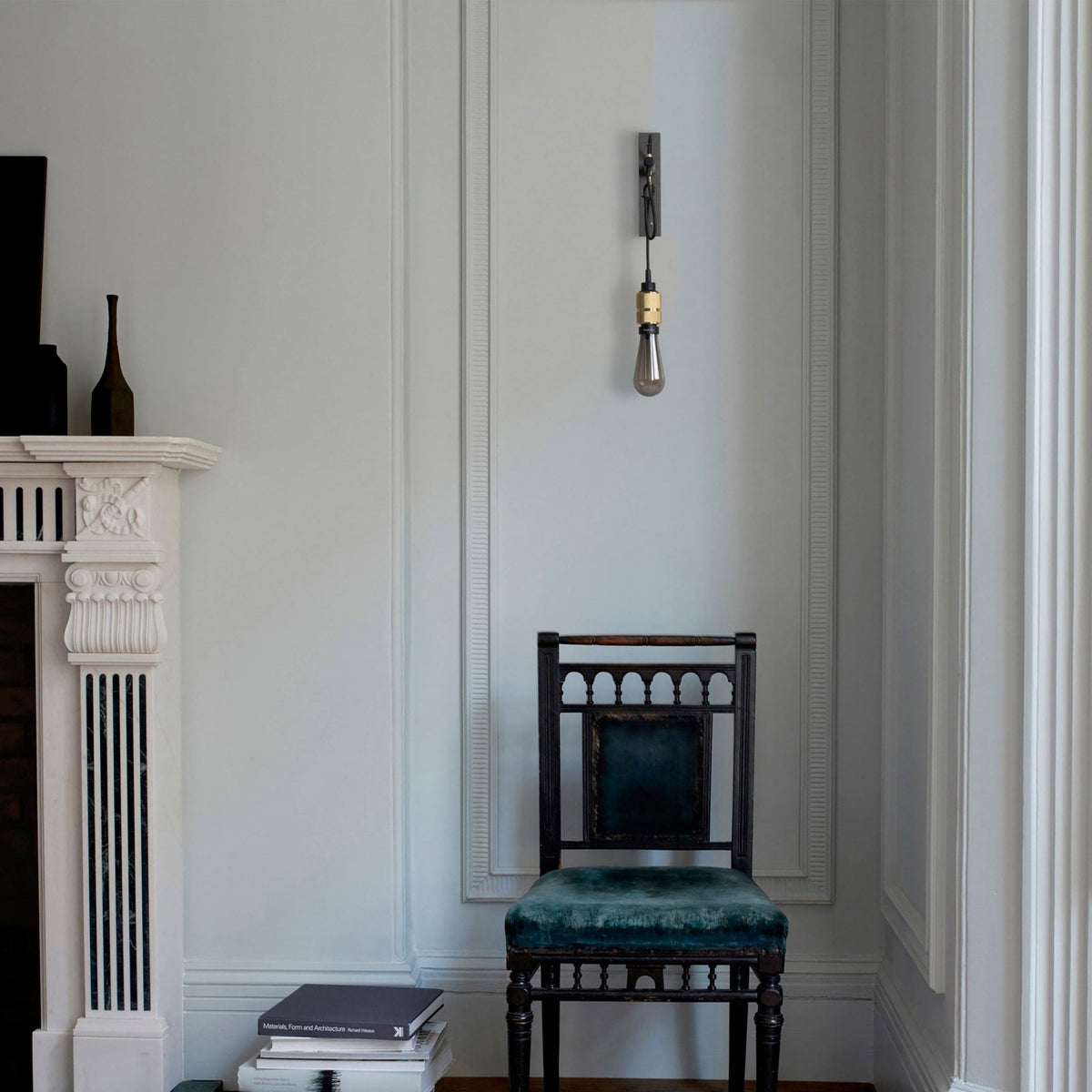 A dark wooden chair with a teal velvet seat and backrest sits next to a white fireplace with black accents.