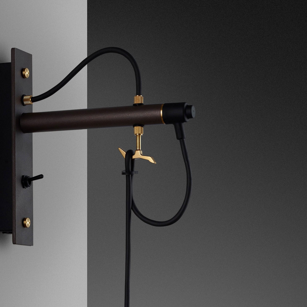 Close-up of a wall-mounted light fixture with a dark brown arm, black cables, and brass accents. 