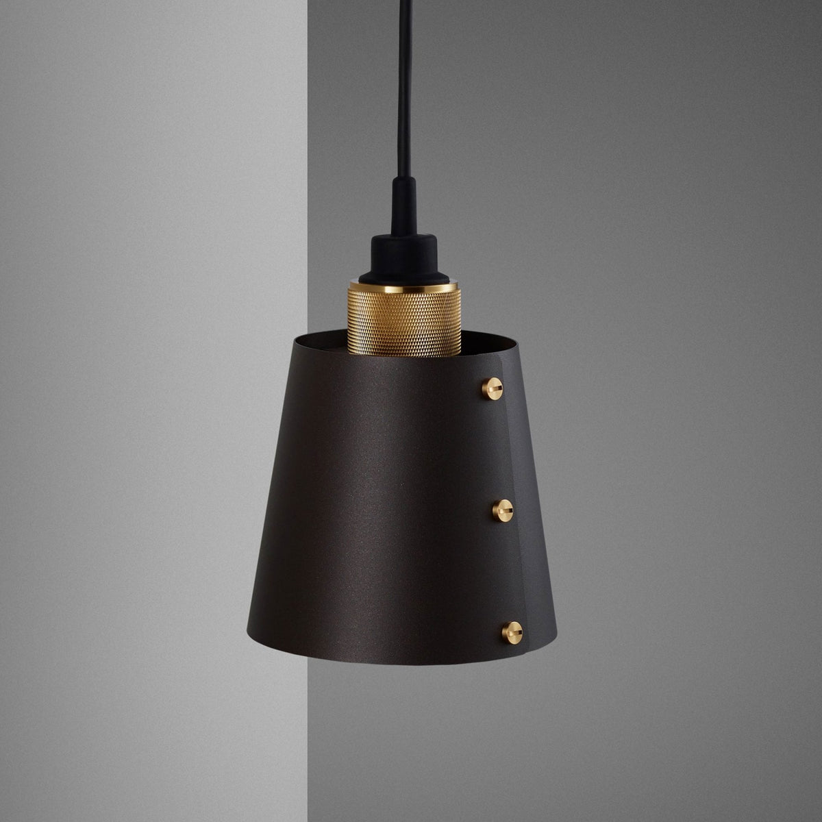 A black pendant light with a textured brass fitting and three brass screws on the shade.