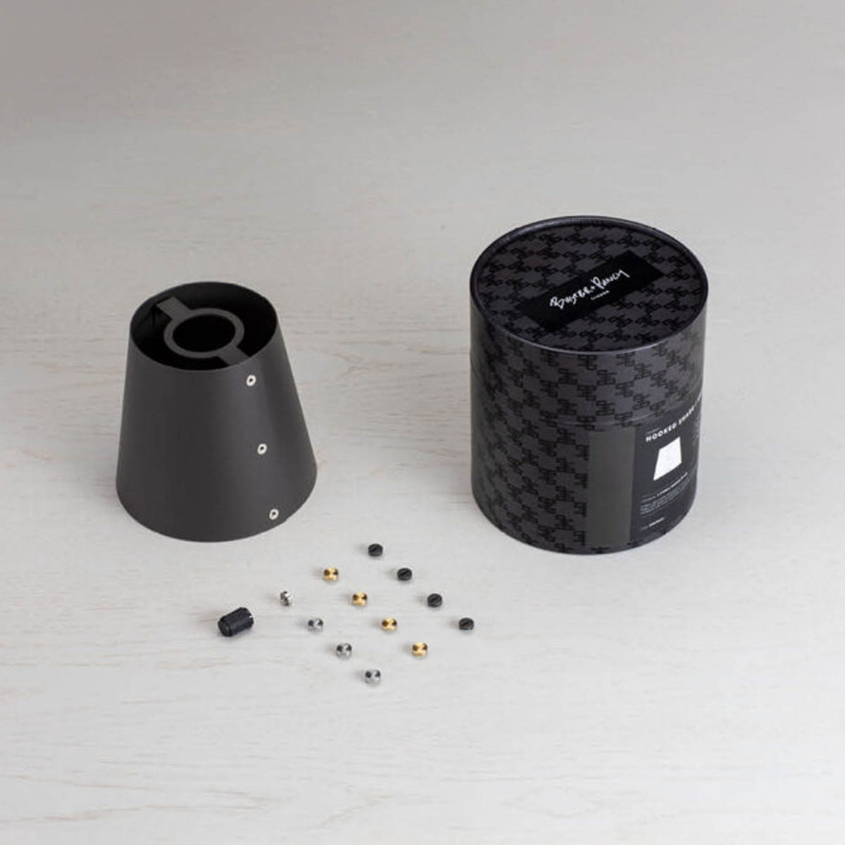 Black conical lamp shade, small gold and silver screws, and a black cylindrical box with a pattern.
