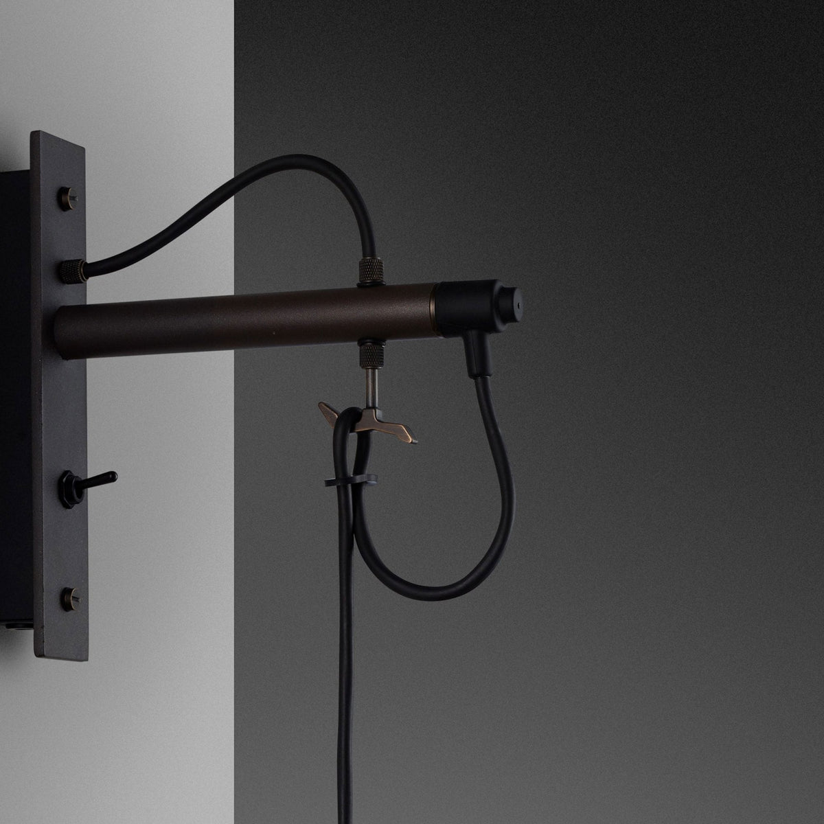 Close-up of a dark bronze wall-mounted light fixture with black wiring and a toggle switch. 