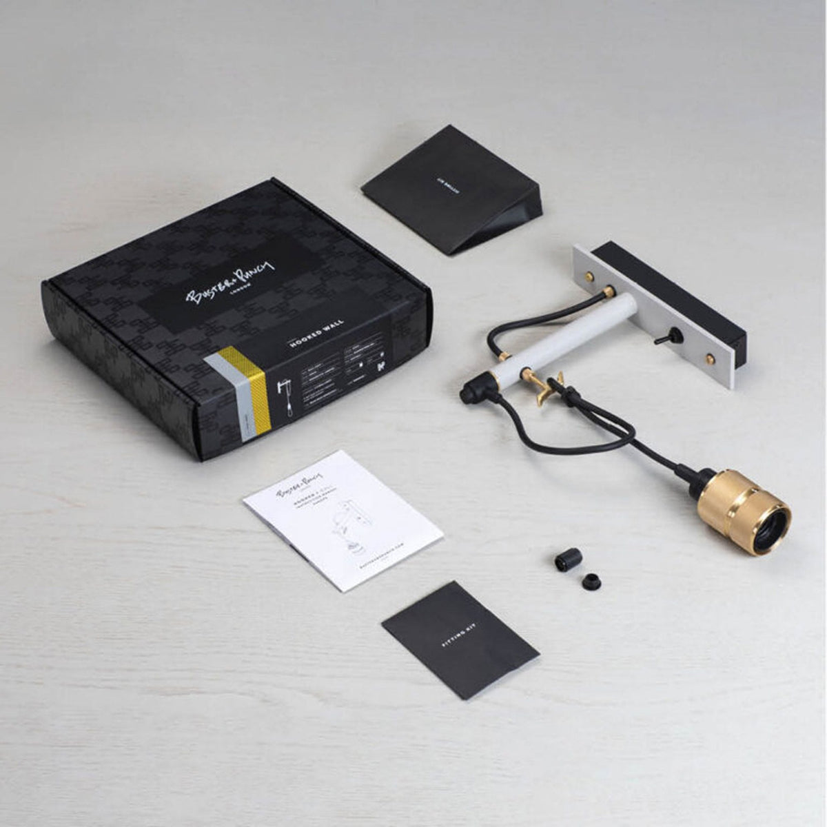 Unboxed Buster + Punch Hooked Wall light with packaging and instructions on a light wooden surface.