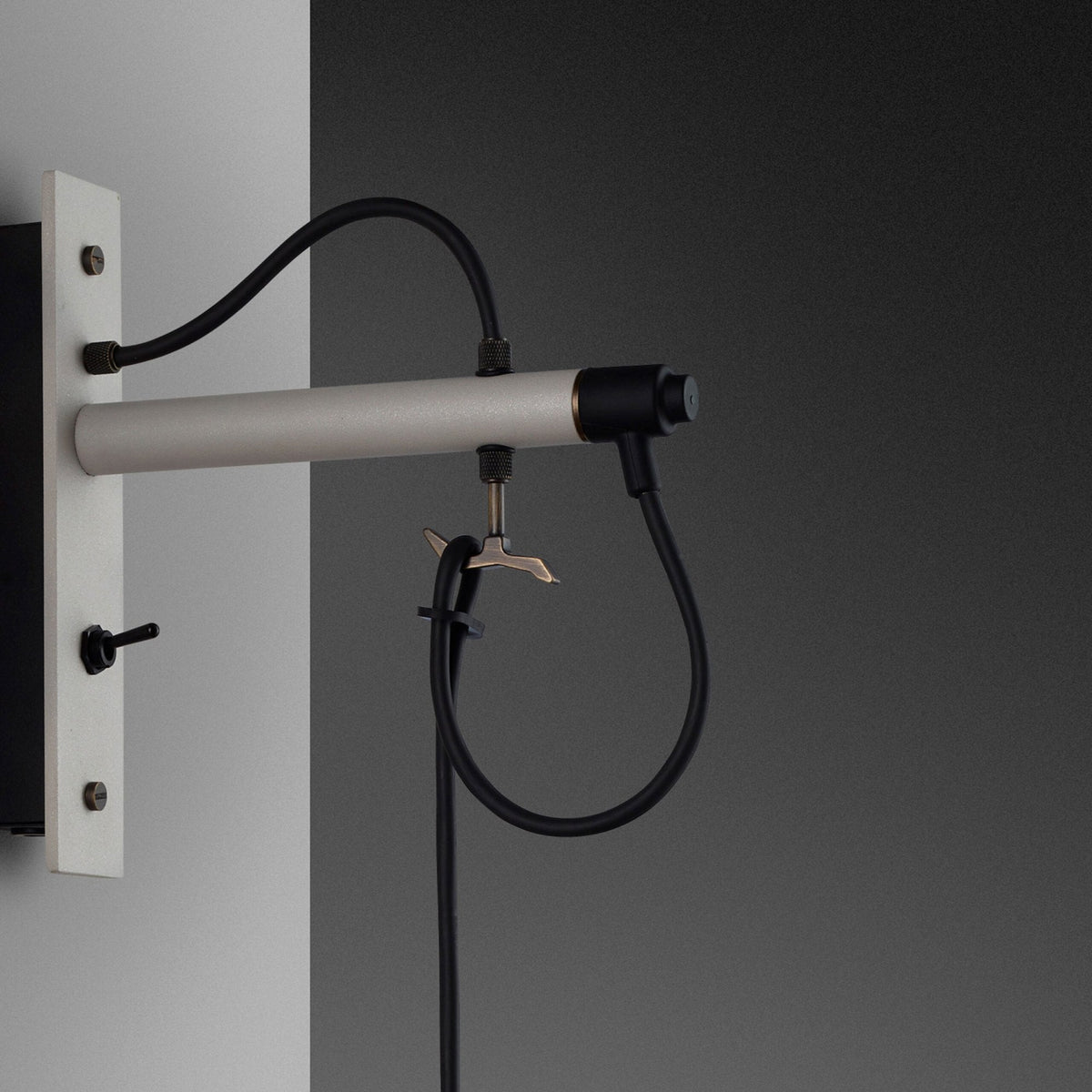 Close-up of a wall-mounted light fixture with a silver arm, black cables, and a small toggle switch.