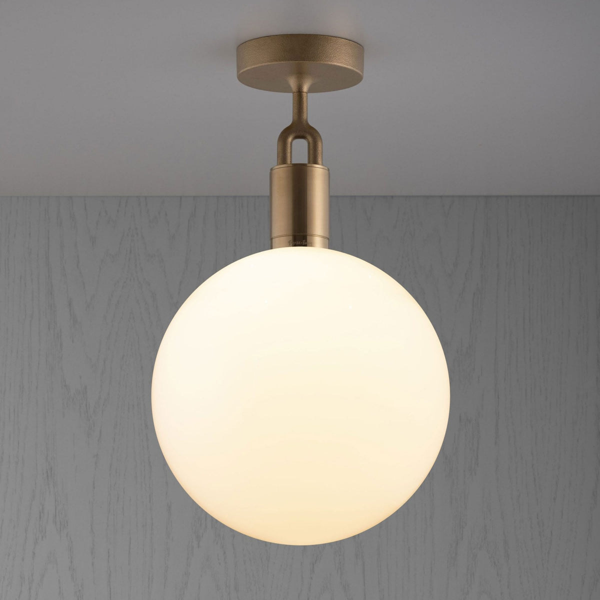 A modern ceiling light with a brass base and a large, glowing spherical white shade.