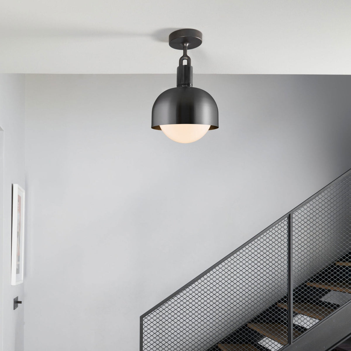 A modern black dome-shaped ceiling light with a frosted globe, illuminating a grey staircase.