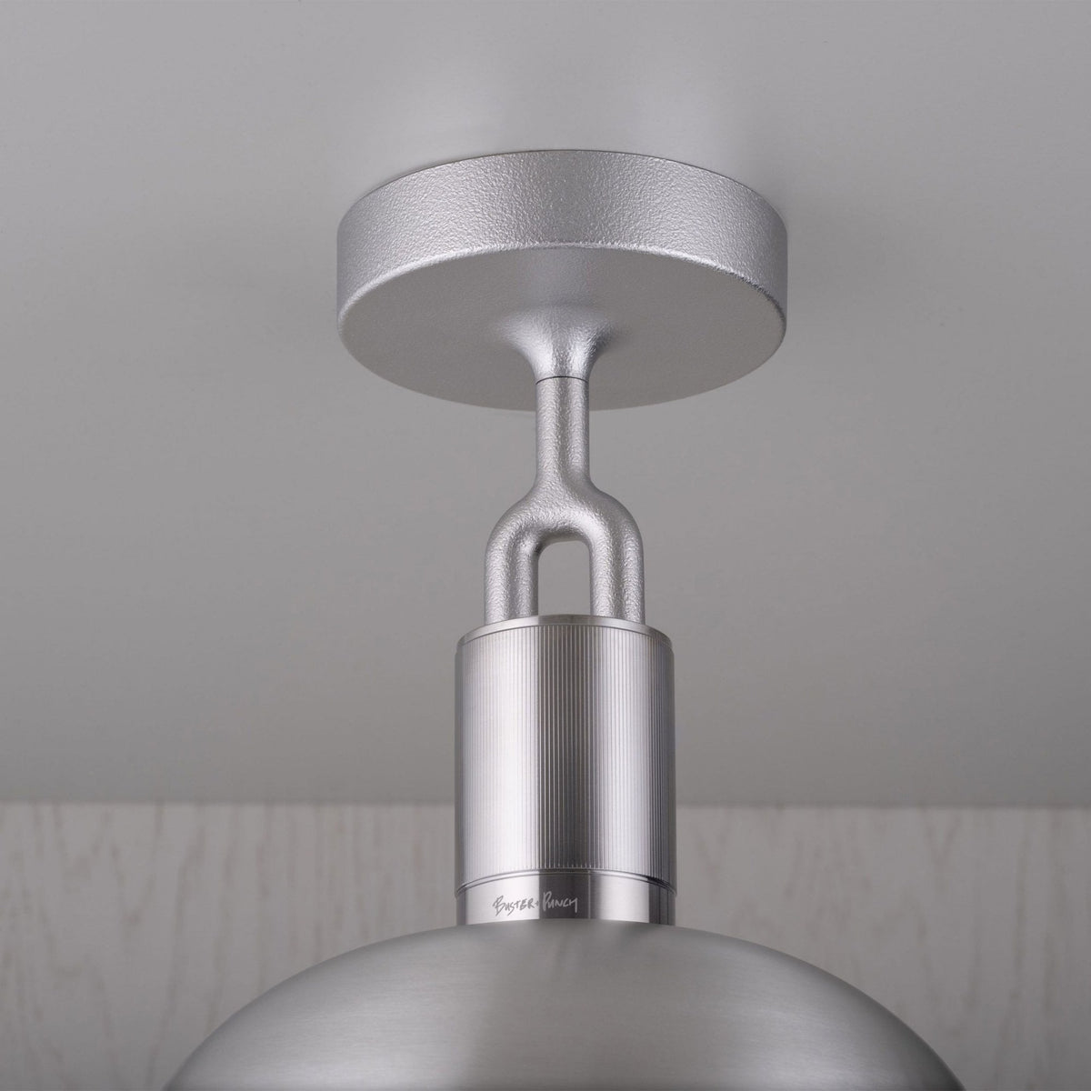 Close-up of a silver ceiling light fixture with a textured finish and a smooth, domed shade.