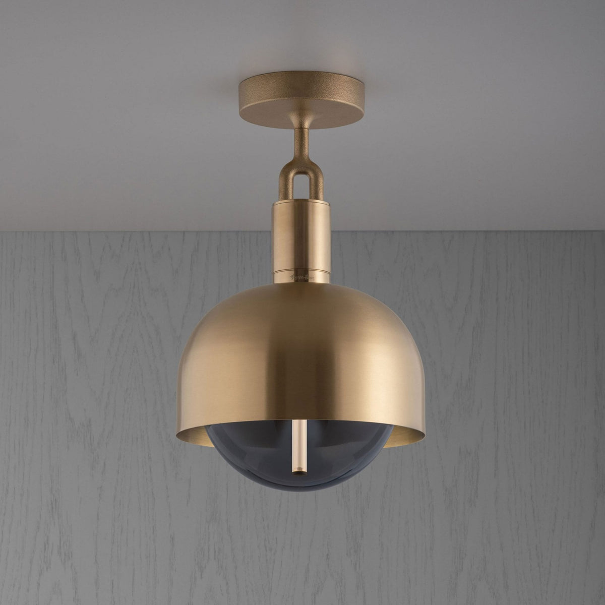 A brass ceiling light with a dome-shaped shade and a dark glass diffuser, mounted on a light grey ceiling.