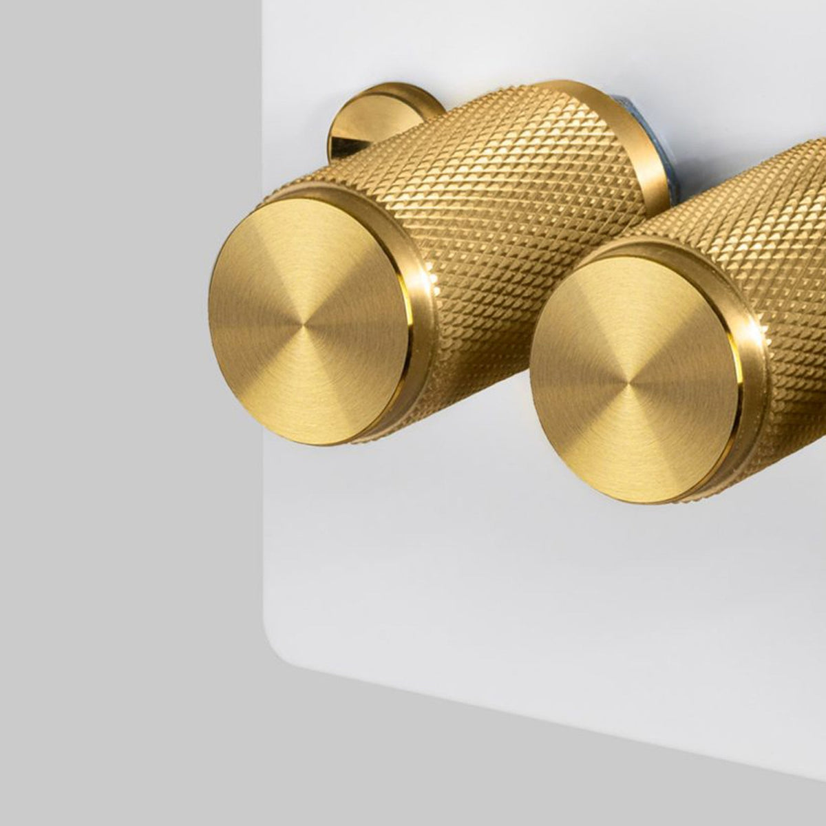 A close up of two brass dimmer knobs with a diamond-cut knurled pattern.