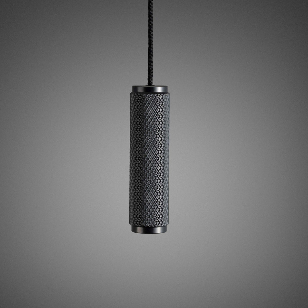 Black cylindrical light pull with a diamond-knurled pattern, hanging from a braided cord against a grey background.