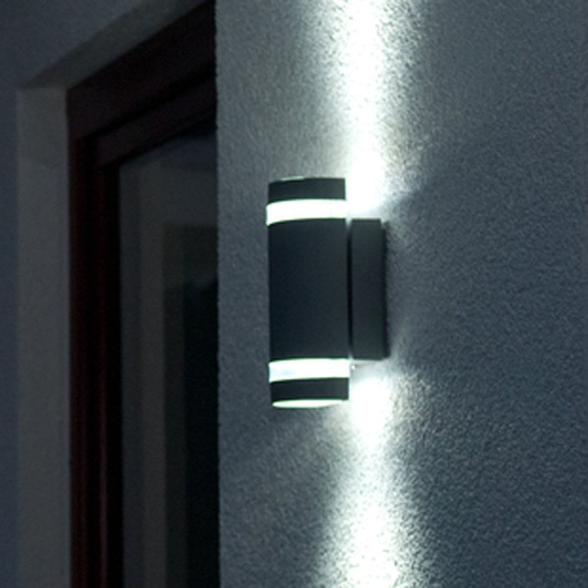 Modern black cylindrical outdoor wall light illuminating a textured wall.