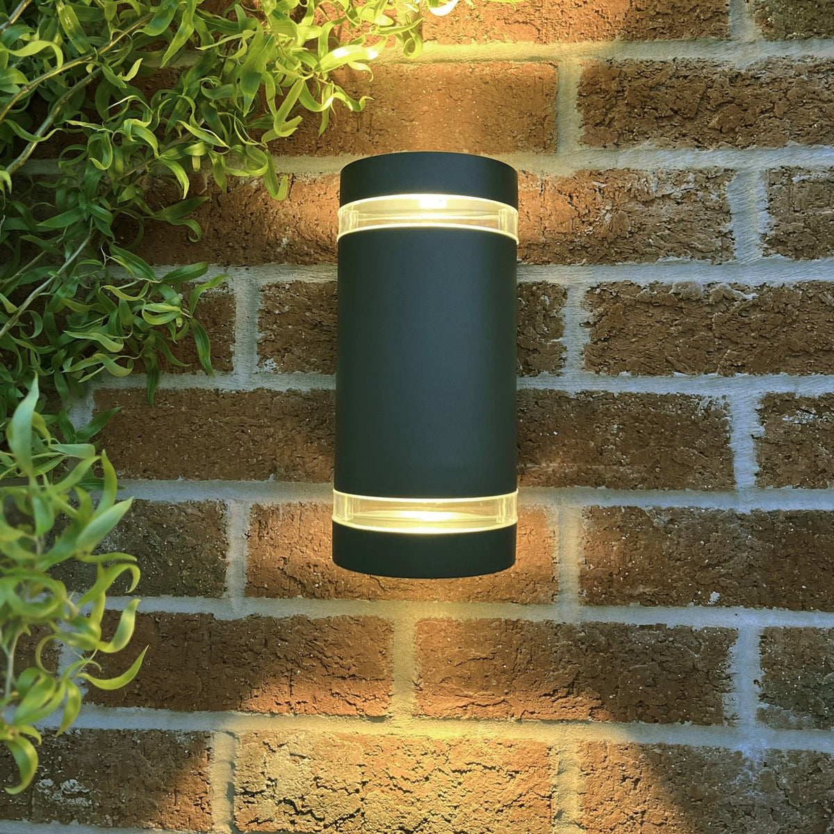 A black up-down outdoor wall light illuminates a brick wall at night.