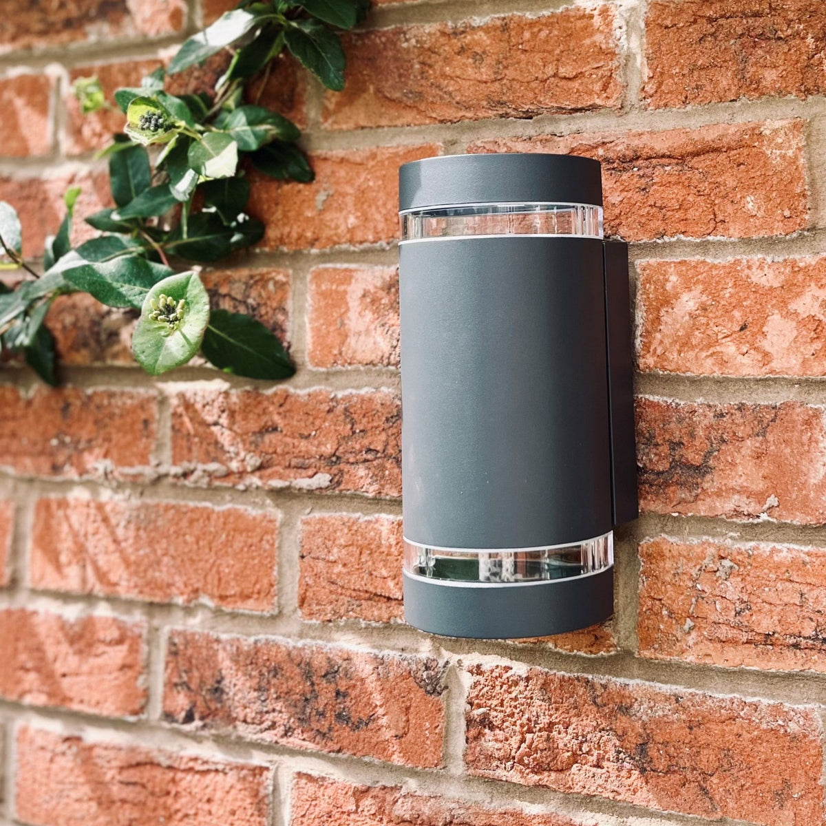 A black up-down outdoor wall light on a brick wall during the day.