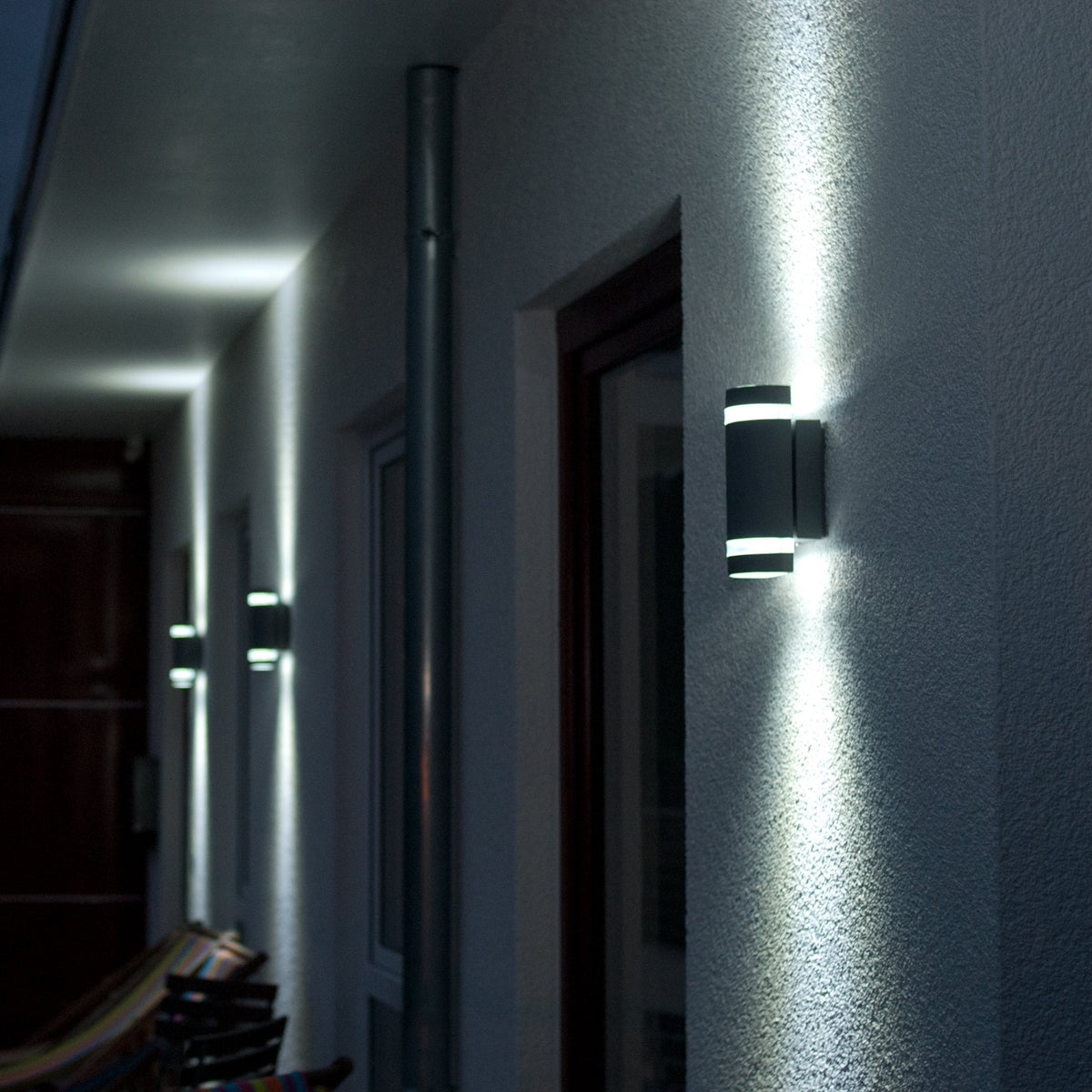 Multiple up-down wall lights illuminate an outdoor corridor at night.