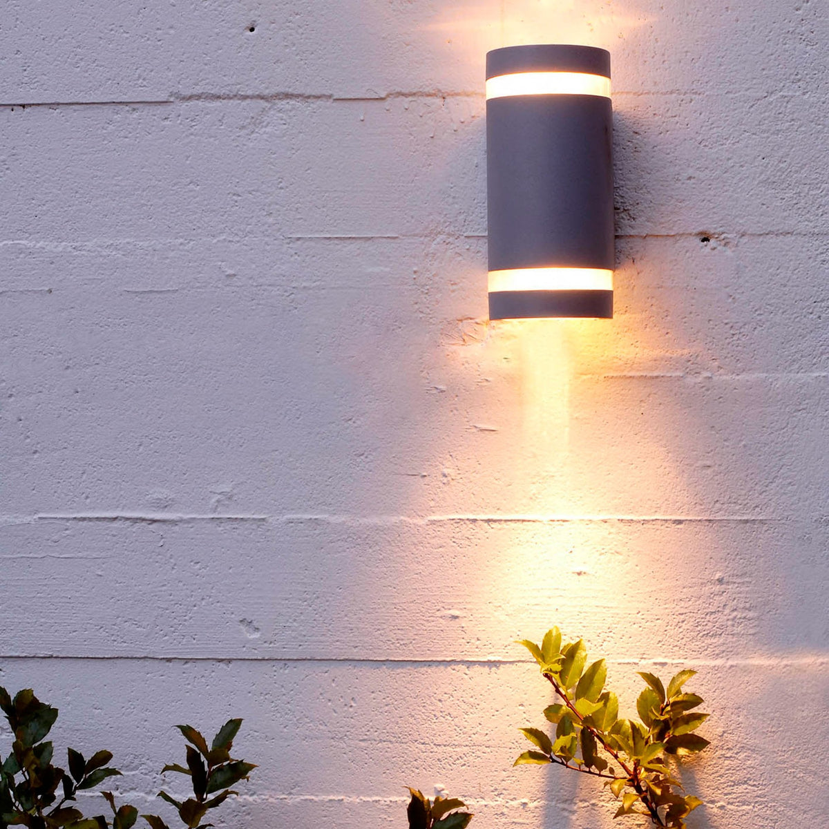 An up-down wall light on a grey wall at night, casting light upwards and downwards.