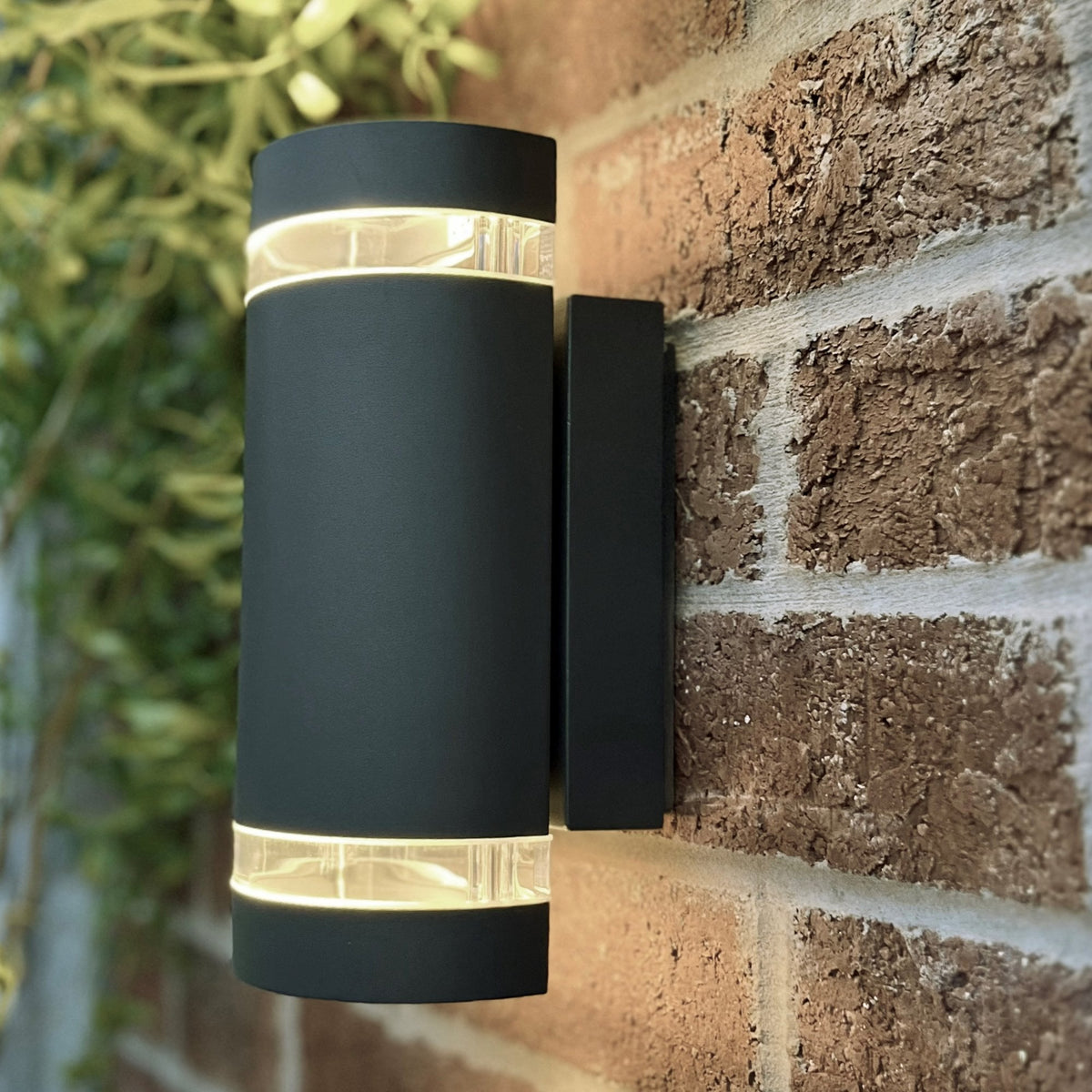 A black up-down outdoor wall light with two clear bands, on a brick wall.