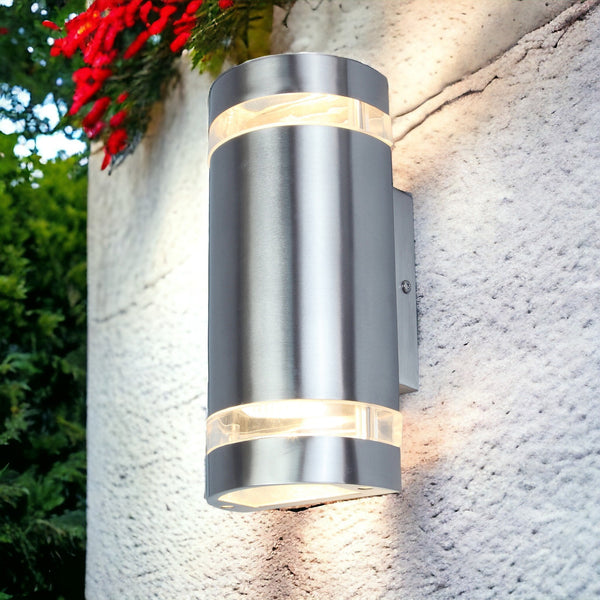 A modern outdoor light illuminating a white wall, with a vibrant red flower above it.
