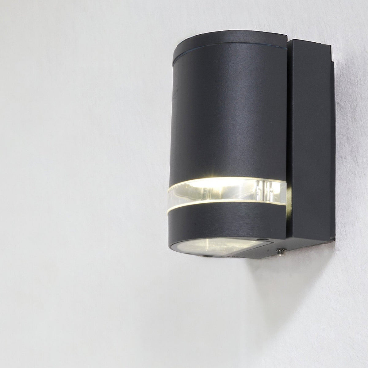 Black cylindrical outdoor wall light with clear band and illuminated top and bottom sections, mounted on a white wall.