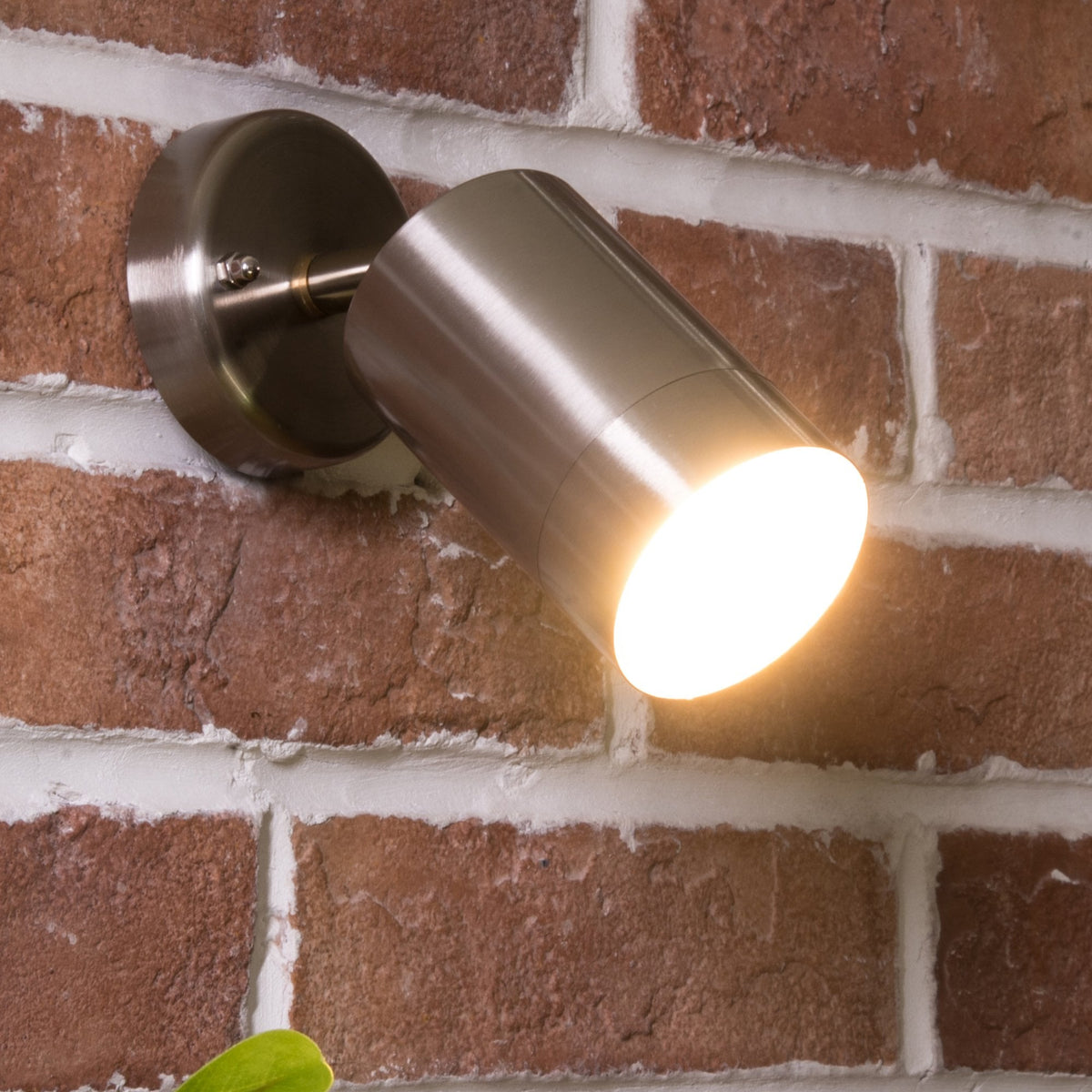 A brushed metal spotlight illuminates a textured brick wall, highlighting its rustic charm and warm tones.