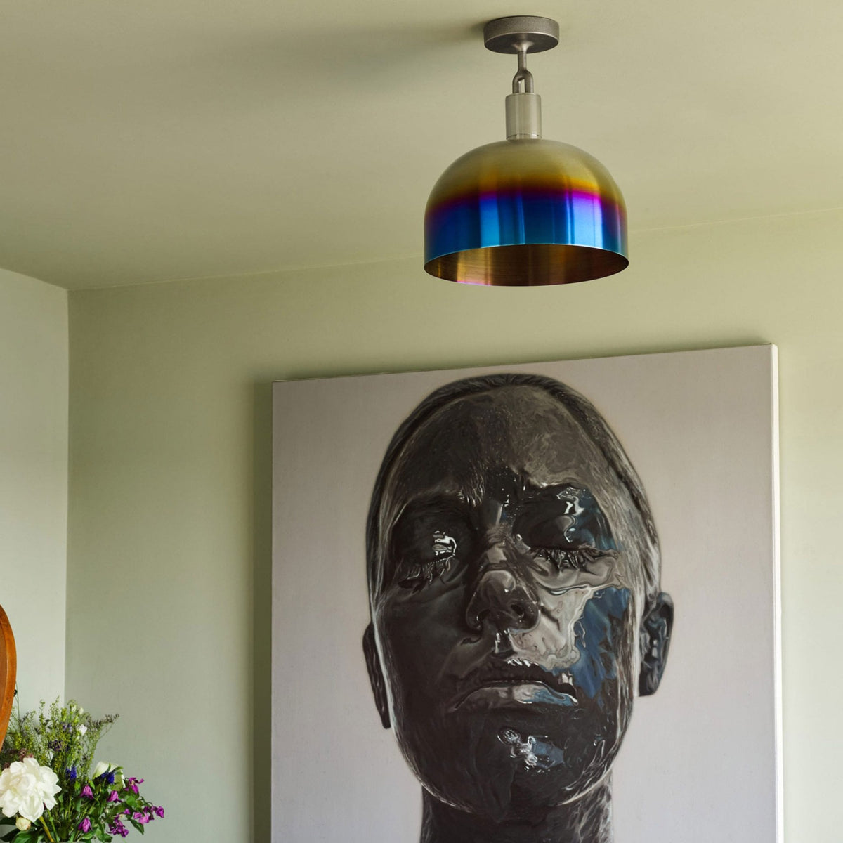 A dome-shaped ceiling light with a vibrant blue and purple iridescent finish, above a modern art portrait.