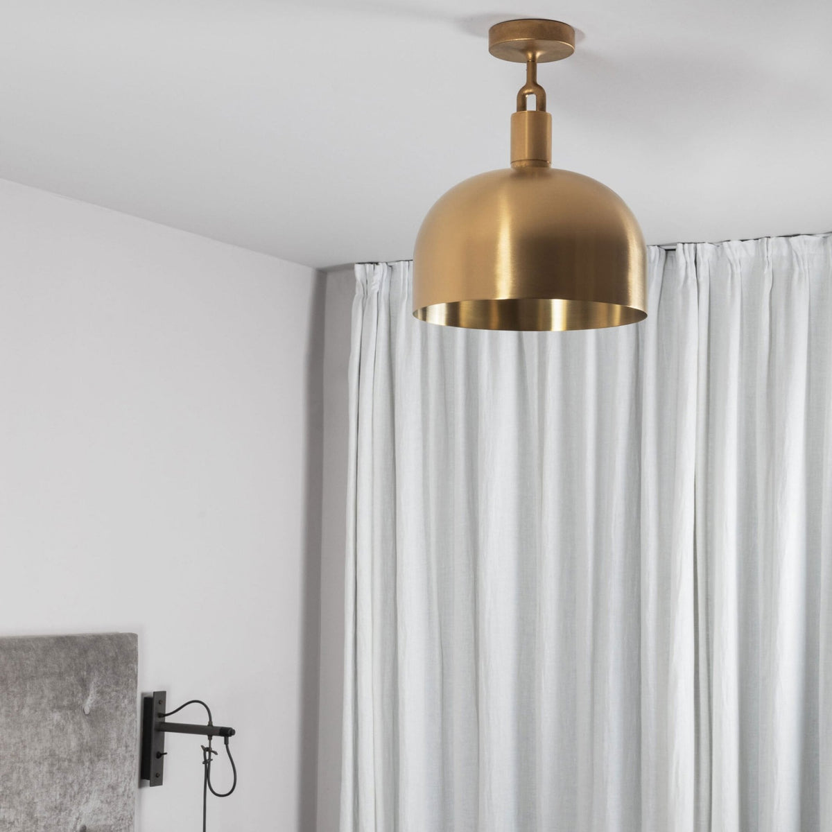 A brass dome-shaped ceiling light hangs in a room with white walls and light-colored curtains.